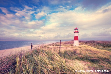 ein Leuchtturm auf einer Düne, im Hintergrund das Meer