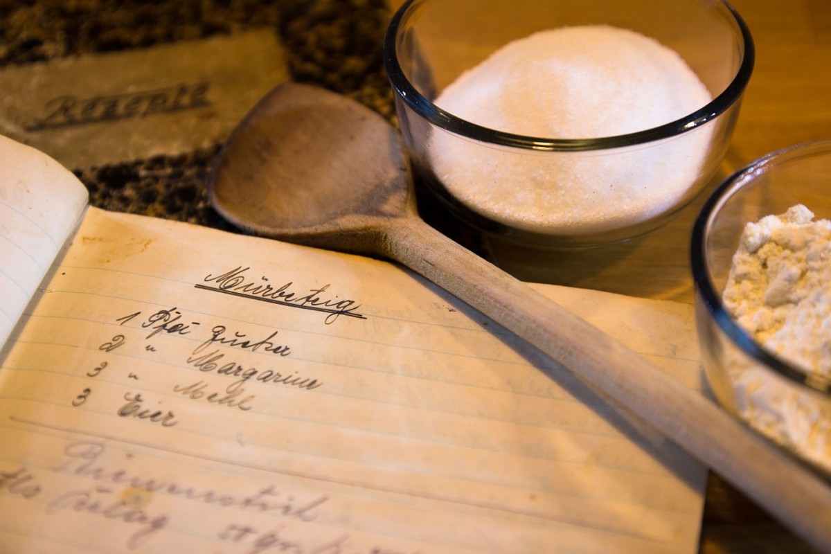 Backzutaten (Zucker, Mehl) und ein altes Rezeptbuch